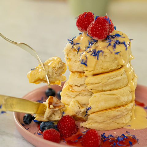 Stapel fluffiger veganer Reoat-Pancakes mit Himbeeren und Blaubeeren als Toppings, es wird ein Stück mit Messer und Gabel weggenommen - SEO-optimiert für Reoat.