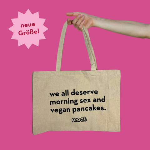 Rechteckiger Jutebeutel mit dem Spruch: 'We all deserve morning sex and vegan pancakes'. Der Beutel wird von einem schlanken Arm gehalten. Alles vor einem pinken Hintergrund.