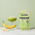 reoat Banana Matcha Haferdrinkpulver als Bio-Getränkepulver in der grünen Packung „reoat BANANA MATCHA HAFERDRINKPULVER“ neben einem cremigen Banana-Matcha-Latte im Coupe-Glas (grün, schaumig, mit Eis), getoppt mit Bananenscheiben; daneben frische Banane und Bananenscheiben auf hellem Marmortisch vor grünem Hintergrund – veganes reoat Latte-Pulver zum schnellen Anrühren (nur Wasser) für Banana Matcha Latte, Iced Matcha, fruchtige Kaffee-Alternative und reoat Drinks-Kollektion.