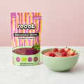 reoat Breakfast Bowl Erdbeer-Himbeer als Bio-Hafermischung („reoat BREAKFAST BOWL ERDBEER-HIMBEER“, „Nur Wasser drauf & fertig“) neben einer Schale rosafarbener Strawberry-Raspberry Porridge/Breakfast Bowl, getoppt mit frischen Himbeeren, halbierten Erdbeeren und Samen/Topping; Szene auf hellem Marmortisch vor rosé Hintergrund – vegane reoat Frühstücksbowl zum schnellen Anrühren nur mit Wasser, fruchtige Bowl für Frühstück, Snack und Meal-Prep, ideal für Bowl-Lover und Fans von Erdbeer-Himbeer-Porridge.