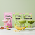 reoat Produktbild der Bio Latte-Getränkepulver als Set: Pink Chai Pulver (rosa Drink im Glas, mit Zimtstange), Matcha Haferdrinkpulver (grüner Matcha Latte im Coupe-Glas) und Banana Matcha Haferdrinkpulver (grüner Drink mit Bananenscheiben); vor den Packungen liegen Banane und Bananenscheiben, Datteln, Vanilleschote und Blüte – vegane, bio-zertifizierte, glutenfreie reoat Latte-Pulver zum schnellen Anrühren (nur Wasser) für Matcha Latte, Pink Chai Latte und Banana Matcha, ideal für Kaffee-Alternative, Iced 